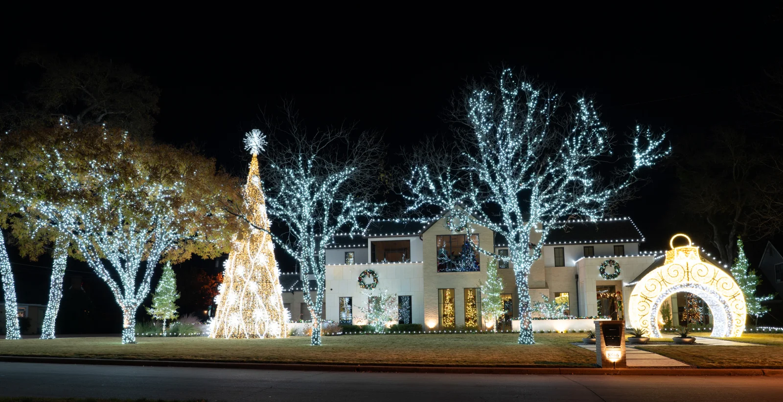 Estate property with multiple mature trees fully wrapped in lights, a custom lit tree sculpture, and a lit walk-through arch, a custom Christmas lighting display by The Perfect Light
