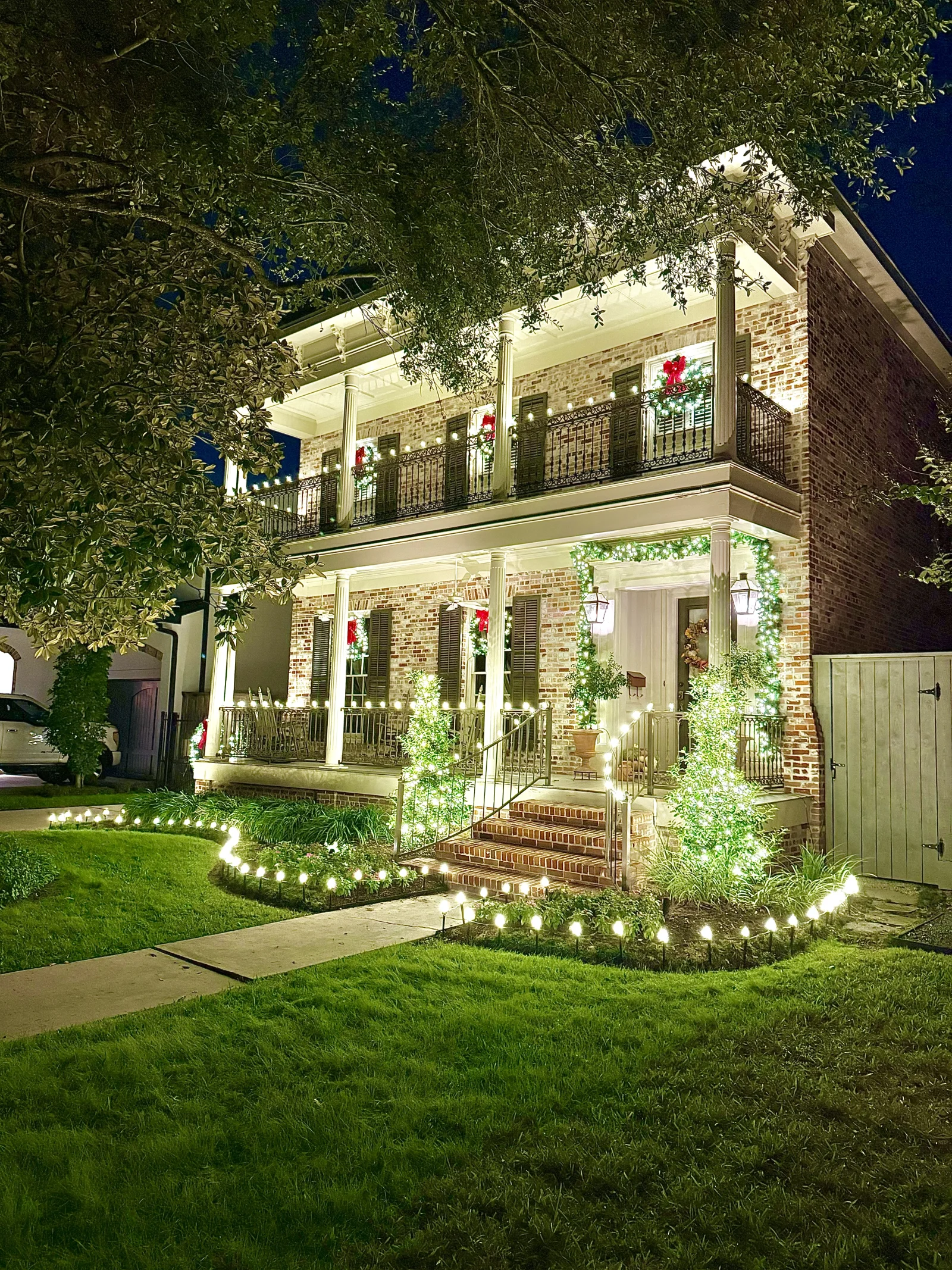 Plantation-style home with a fully wrapped oak tree and garland-wrapped porch columns, a $4,000 Christmas lighting installation by The Perfect Light