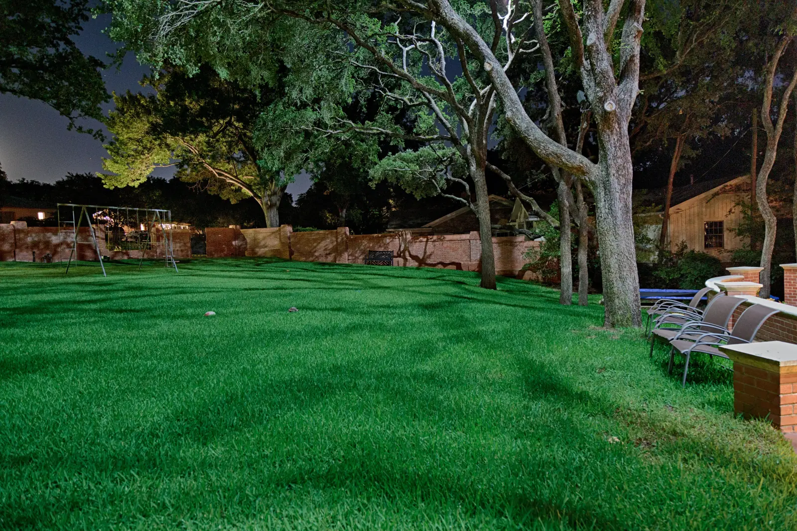Moonlighting landscape lighting technique casting dappled light through a mature oak canopy onto a backyard lawn.