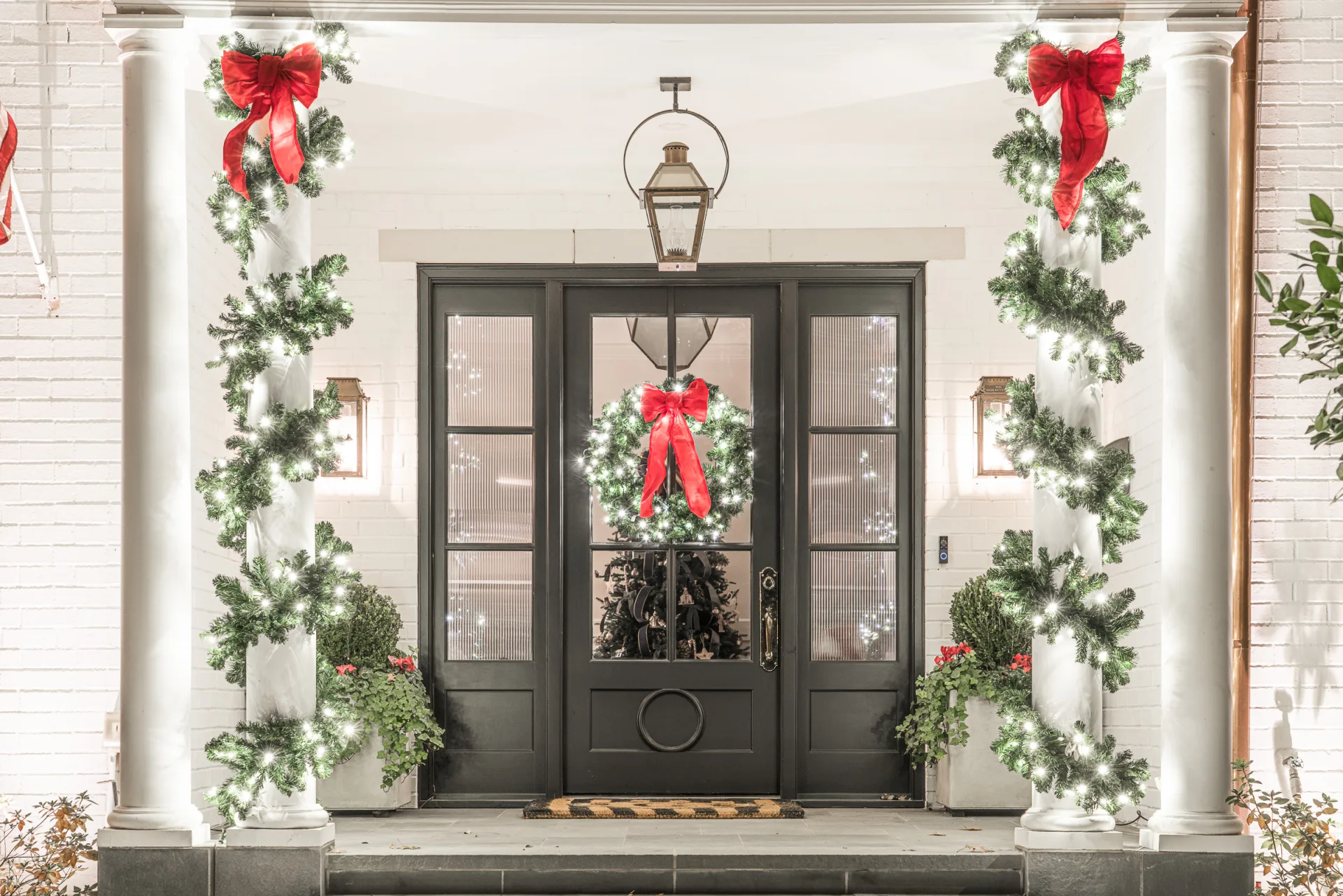 The Perfect Light Christmas lighting on a Texas stone home with lit arch garland, entry trees, and roofline lights at night