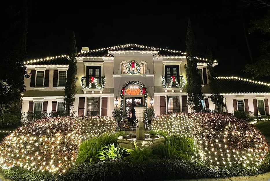 The Perfect Light Christmas lighting on a Texas estate with net-lit shrubs, roofline lights, balcony garland, and a front fountain at night