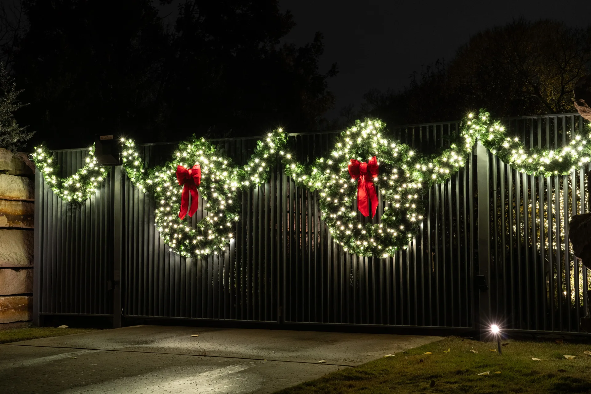 The Perfect Light Christmas lighting on a Texas home with window wreaths, entry garland, roofline lights, and a red wrapped tree at night