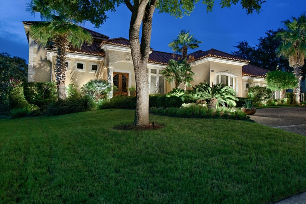 tan home with front landscaping and outdoor lighting