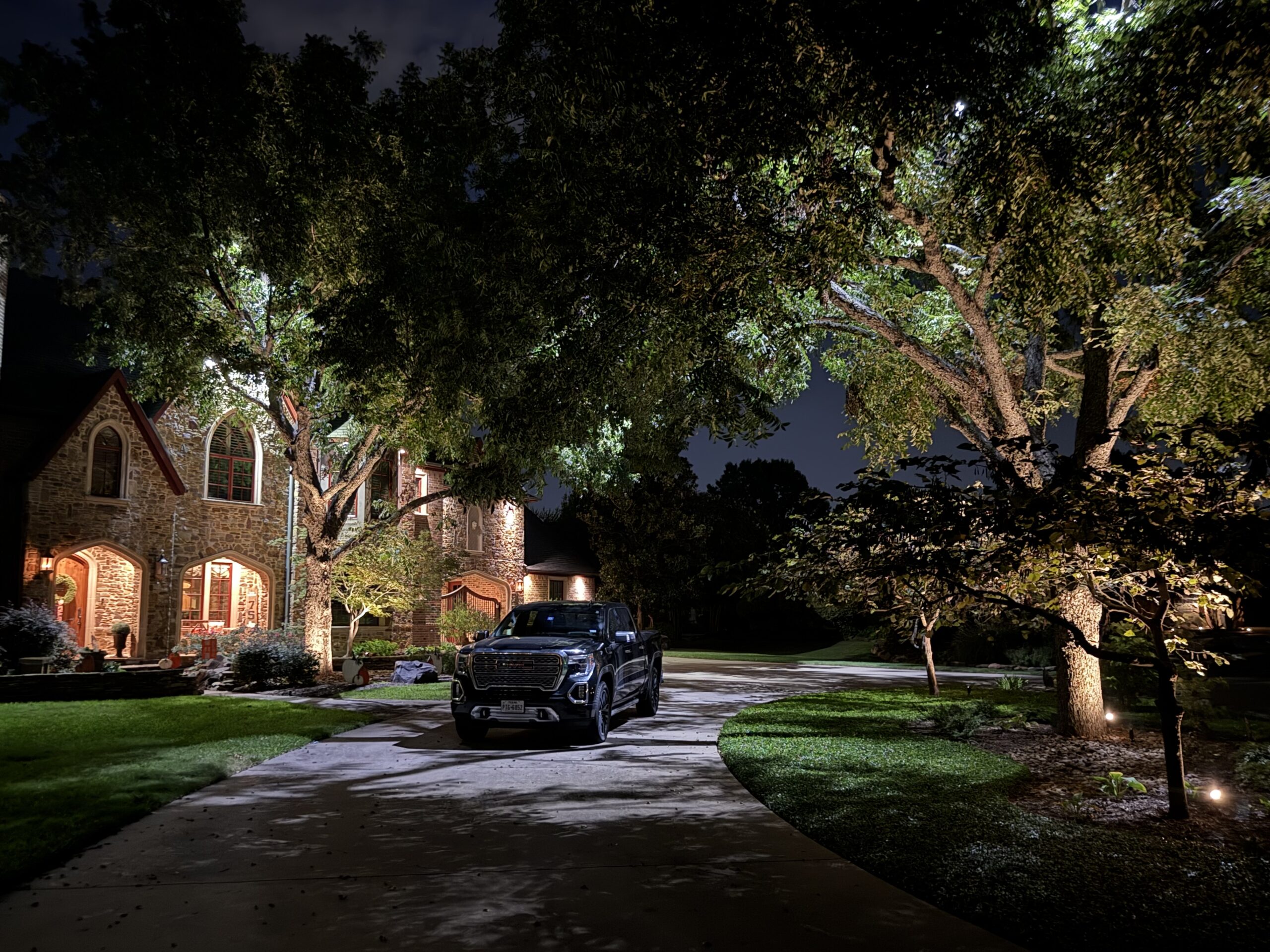 The Perfect Light landscape lighting illuminating a driveway and trees at a Texas home at night